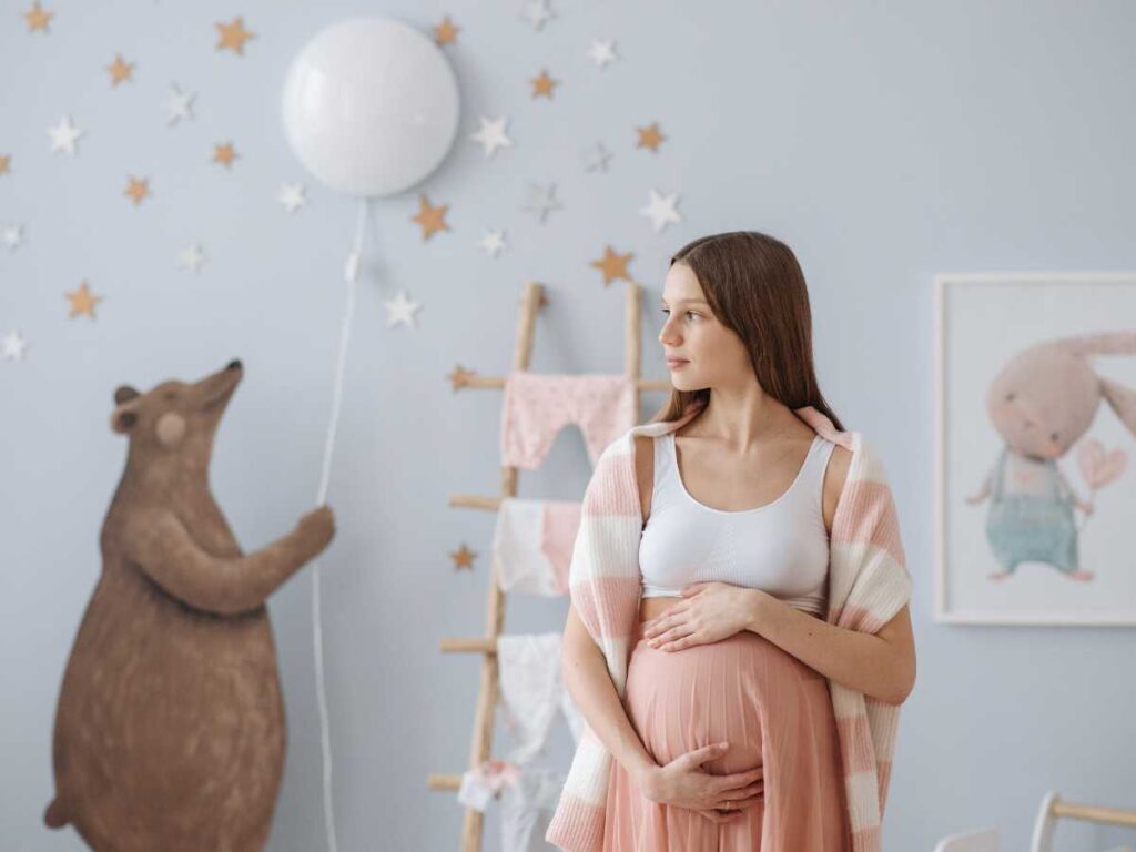 Pregnant woman standing in baby nursery.