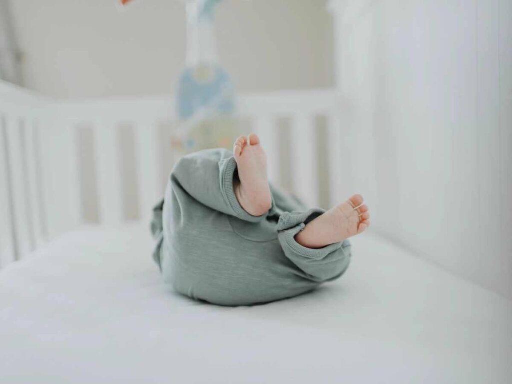 Baby in crib in sage green jumpsuit.