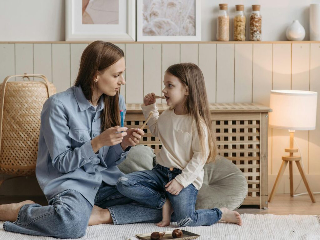 mother sitting with daughter on floor and brushing teeth