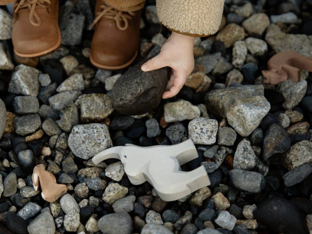 Unrecognizable crop kid playing with toys and stones on rocky ground