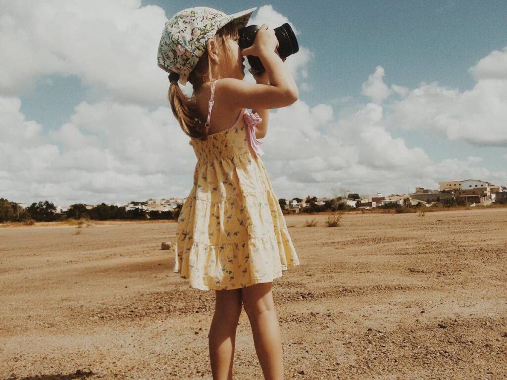 Cute little girl photographing nature on sandy beach