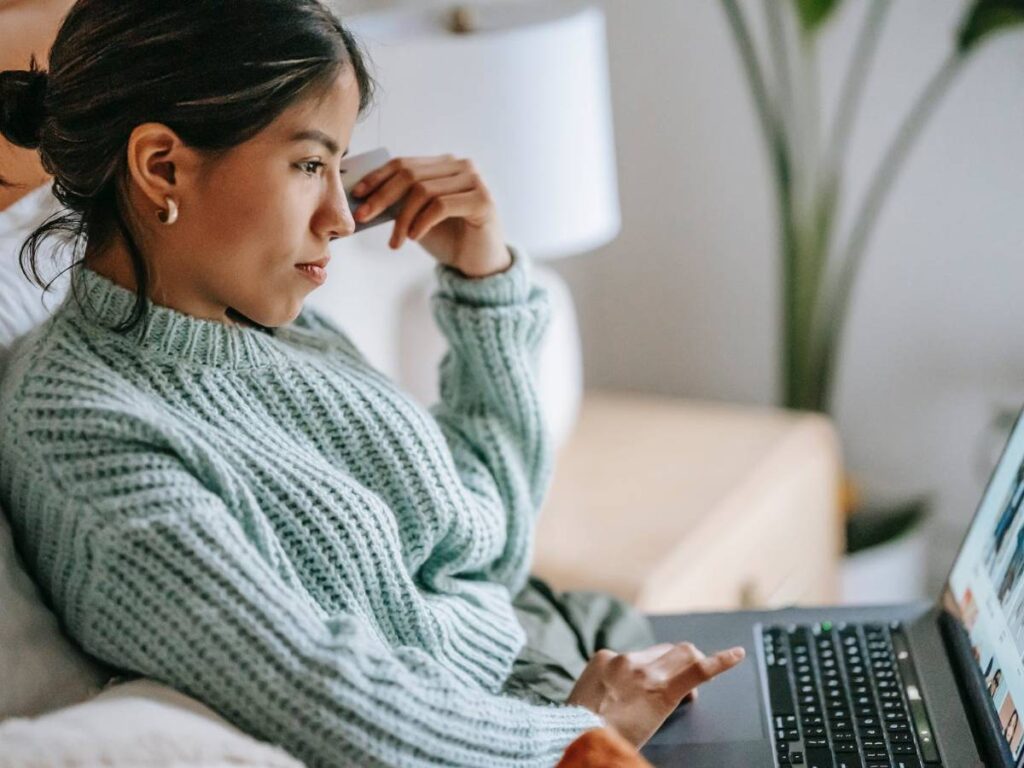 Focused young ethnic woman with credit card and laptop