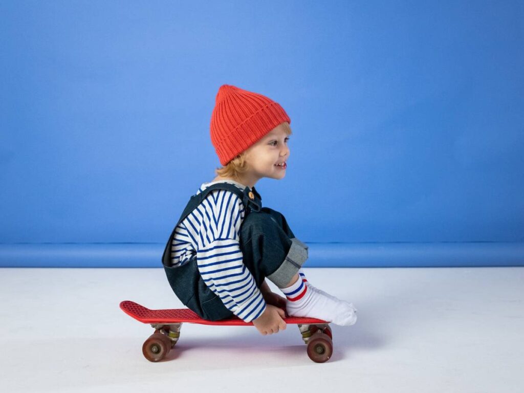 Child in Black and White Striped Long Sleeve Shirt and Red Knit Cap Sitting on Brown
