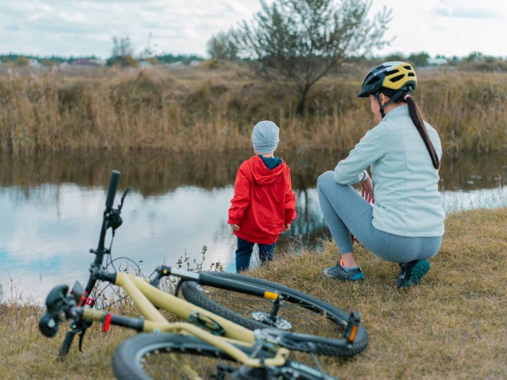 Cyclist Sitting on Riverbank in Field with Toddler