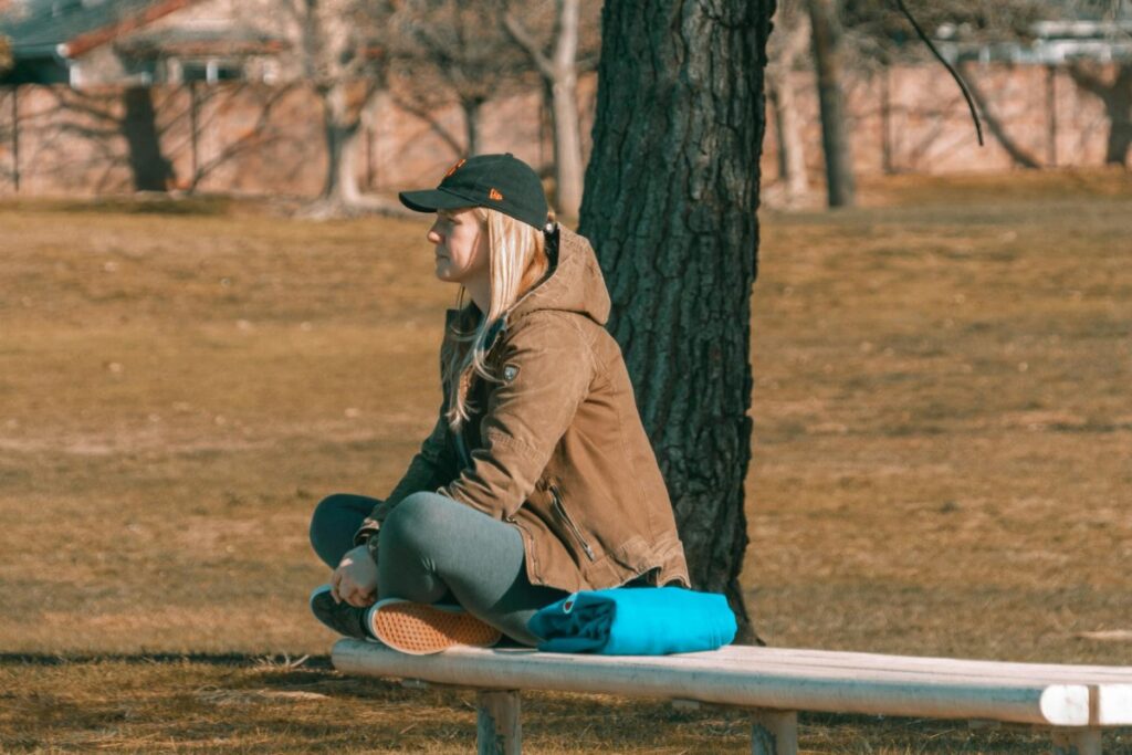 Woman in Cap and Jacket Sitting on Bench at Park
