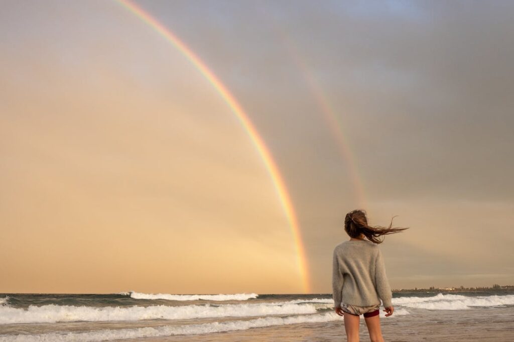 Unrecognizable woman standing on shore with rainbow